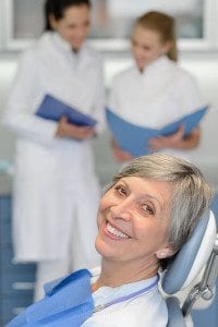 Older Female Laying on Dental Chair With Doctors in Background