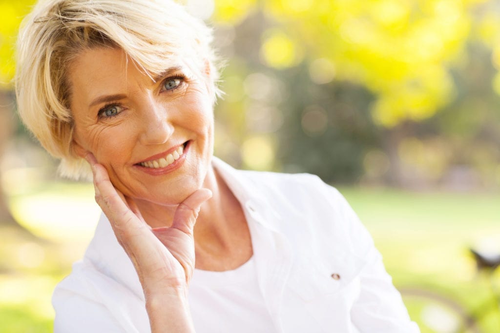 Older Woman Smiling Sitting Outside With Trees